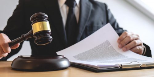 Legal law, advice and justice concept, male counseling lawyer or notary working on a documents and contract papers of the important case and wooden gavel, brass scale in courtroom.